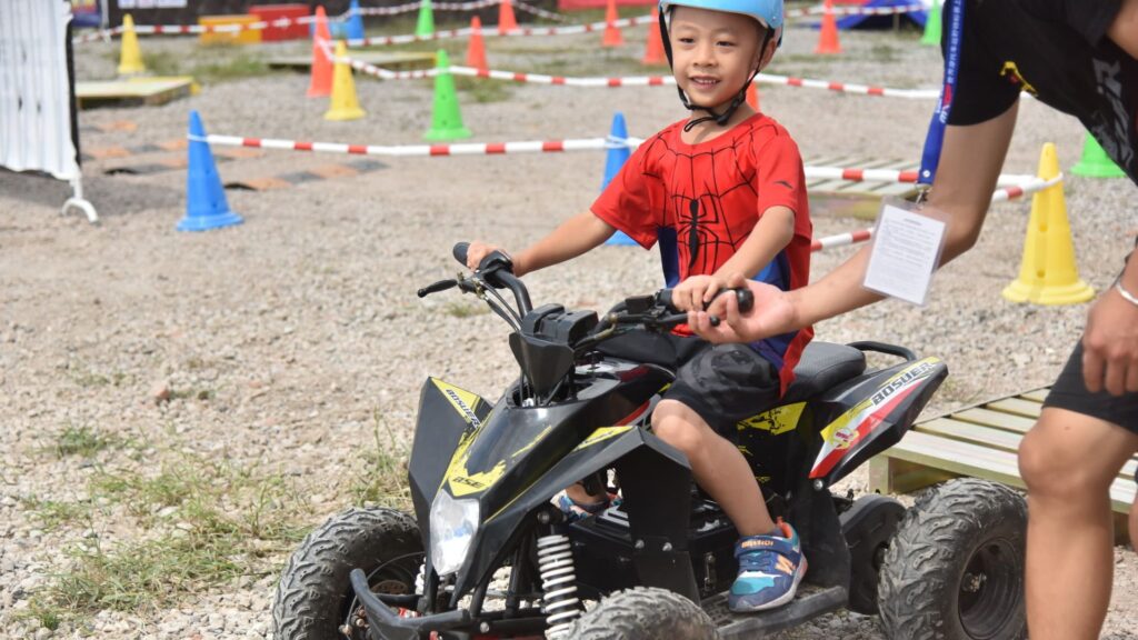 A young kid learning how to ride sport ATV with the help of an adult